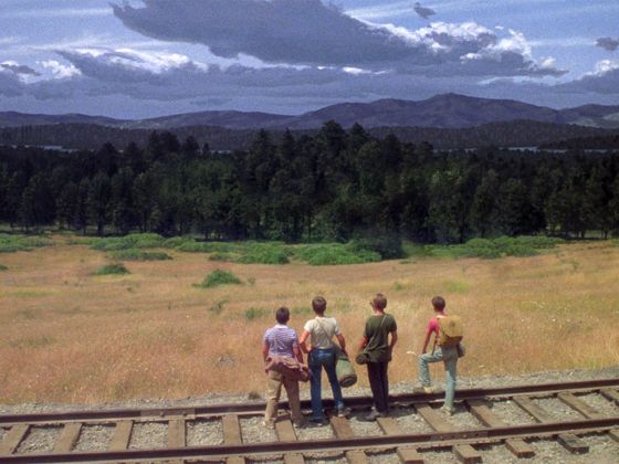 four people standing on train tracks looking out at the mountains and trees in the distance