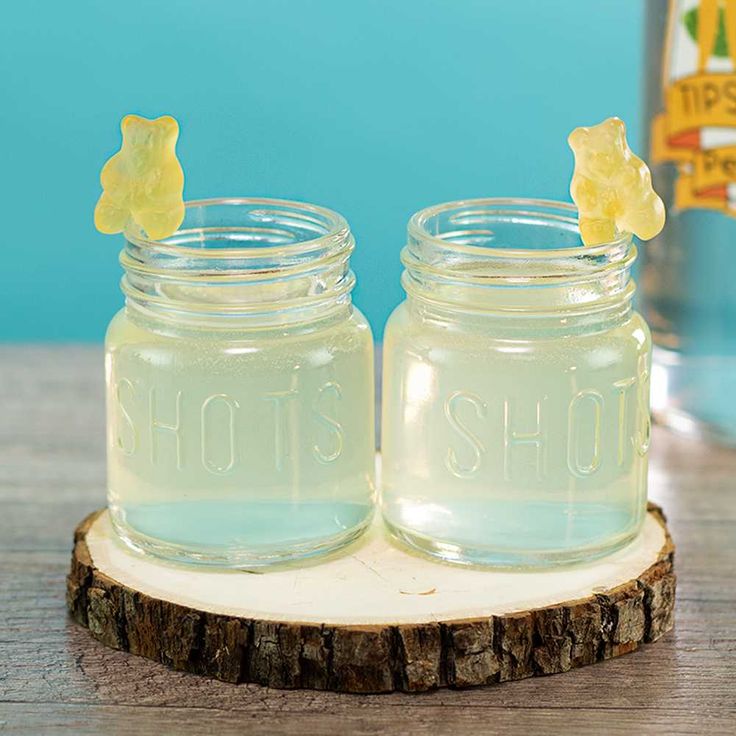 two glass jars with yellow gummy bears in them sitting on a wooden stand next to a bottle