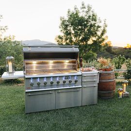 an outdoor bbq grill in the middle of a grassy area with lights on it