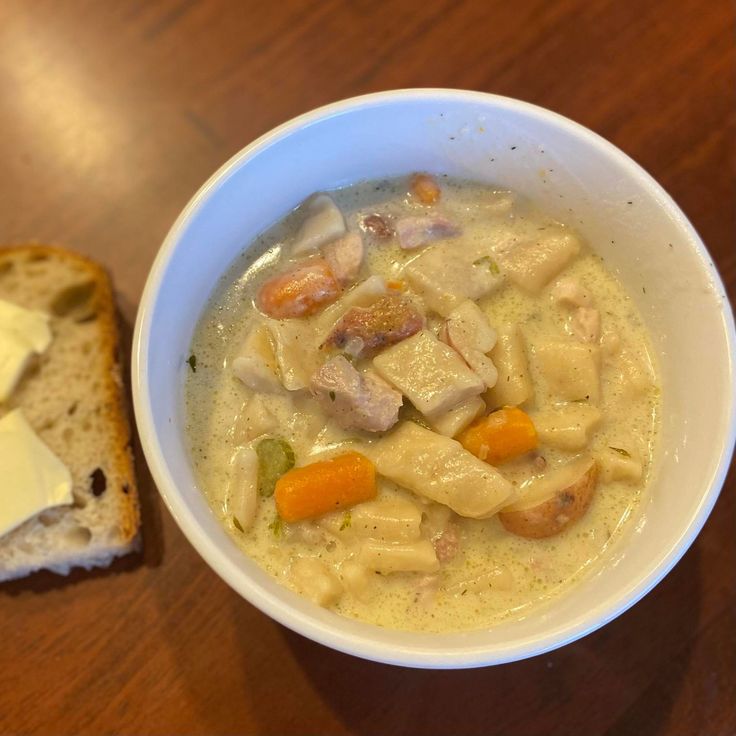 a bowl of chicken noodle soup next to a slice of bread on a table