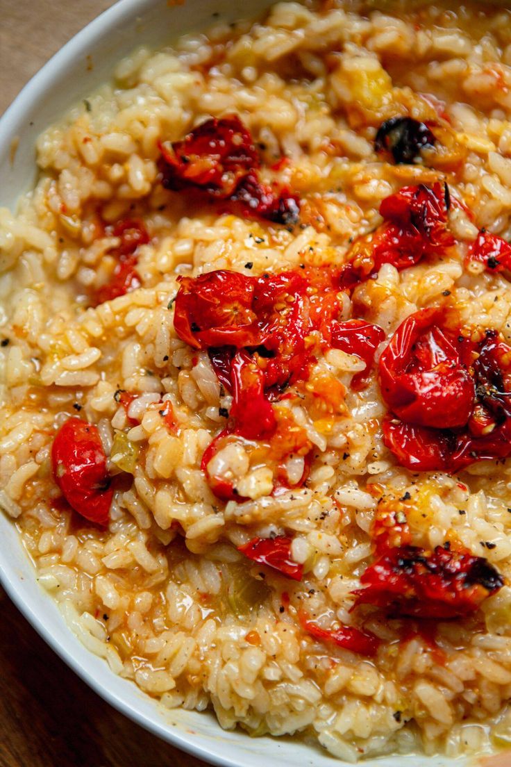 a white bowl filled with rice and tomatoes on top of a wooden table next to a fork