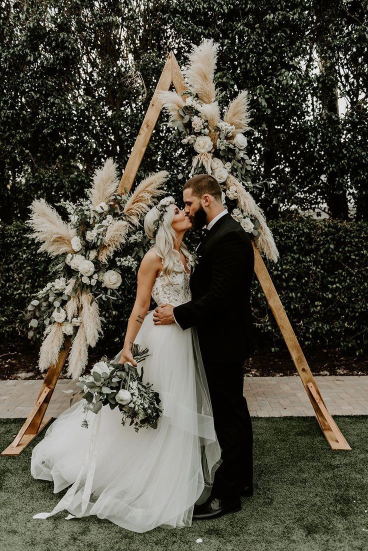 a bride and groom kissing in front of an arch decorated with pamodia flowers