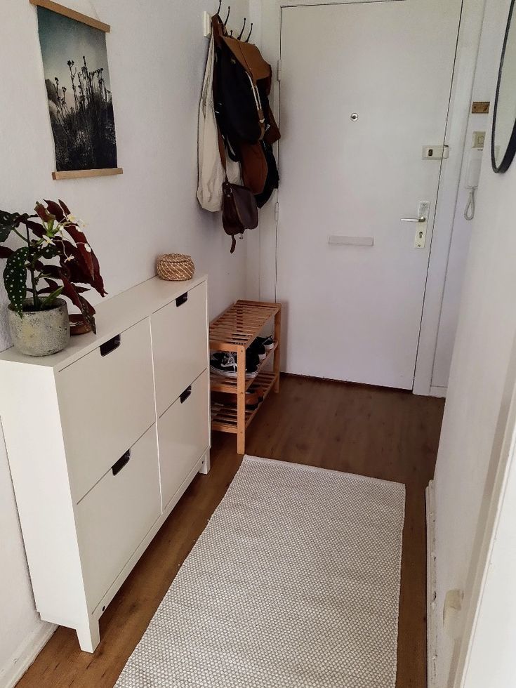 a hallway with white cabinets and wooden flooring, hanging hooks on the wall next to an entryway