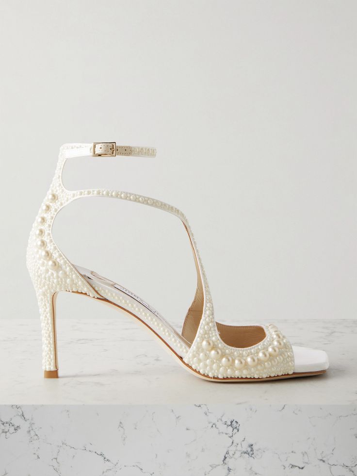 a pair of white high heeled shoes with pearls