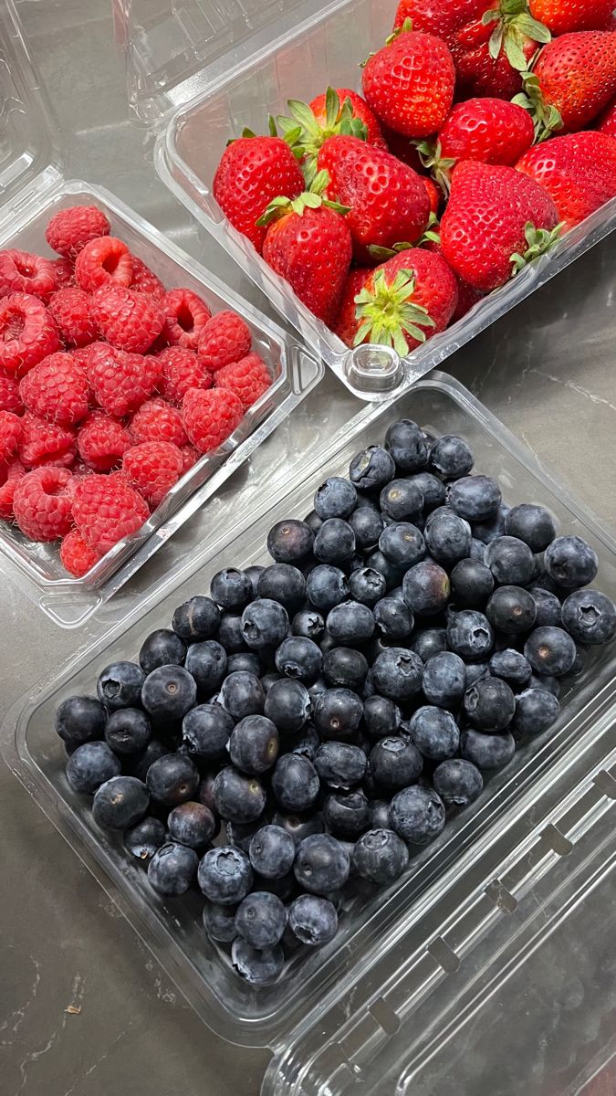 three plastic containers filled with blueberries and strawberries on top of a metal table