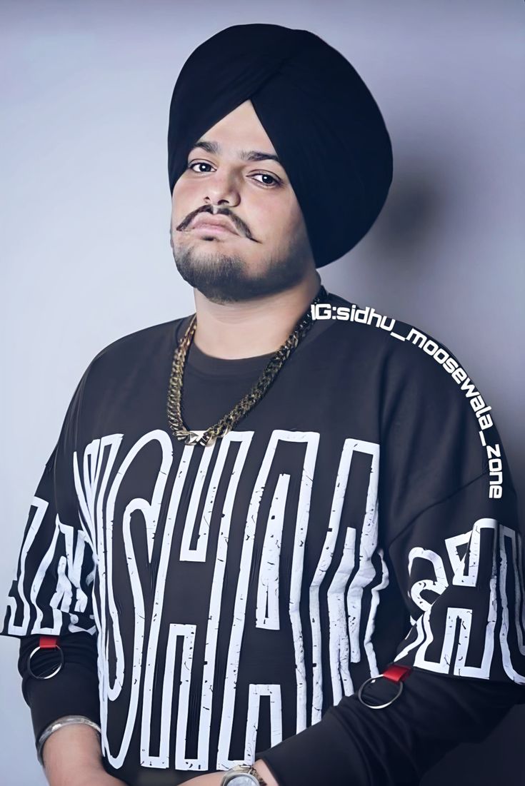 a man with a black turban on his head standing in front of a gray background