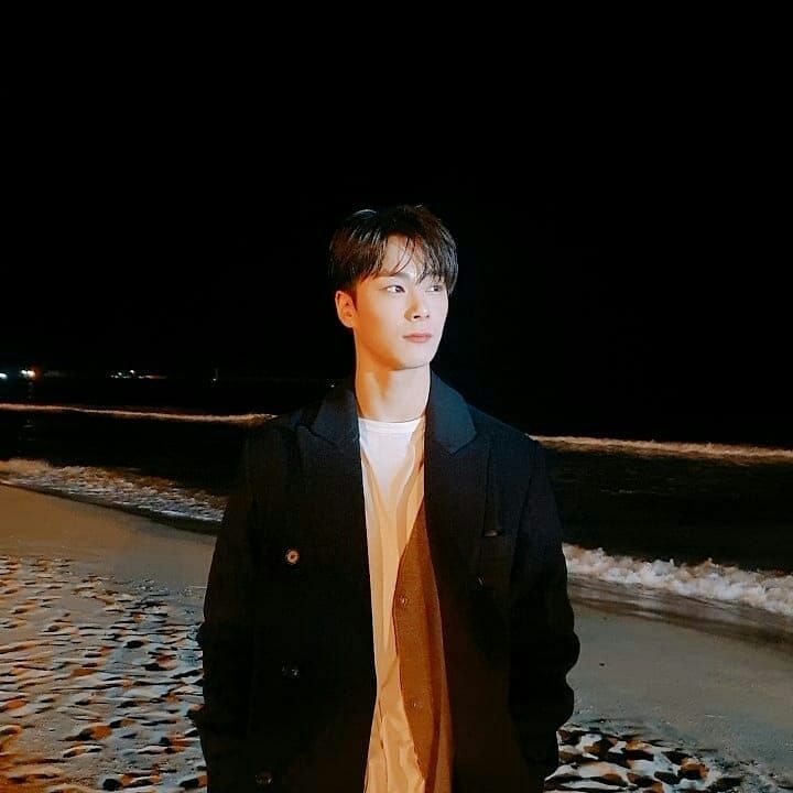 a young man standing on top of a beach next to the ocean in front of a dark sky