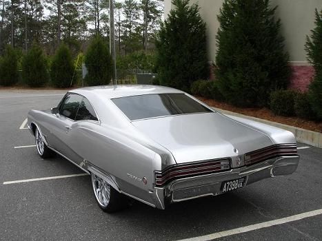 a silver car parked in a parking lot next to a building with trees behind it