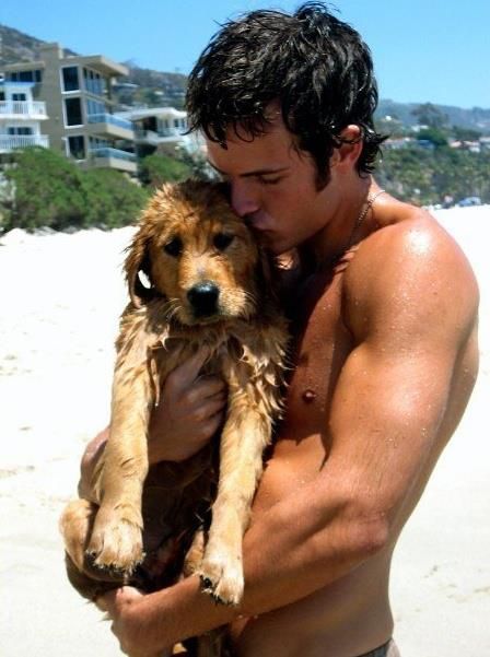 a shirtless man holding a dog on the beach