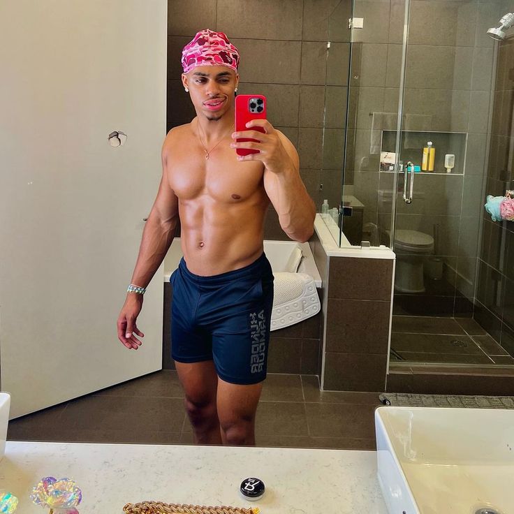 a shirtless man taking a selfie in front of a bathroom mirror with his cell phone