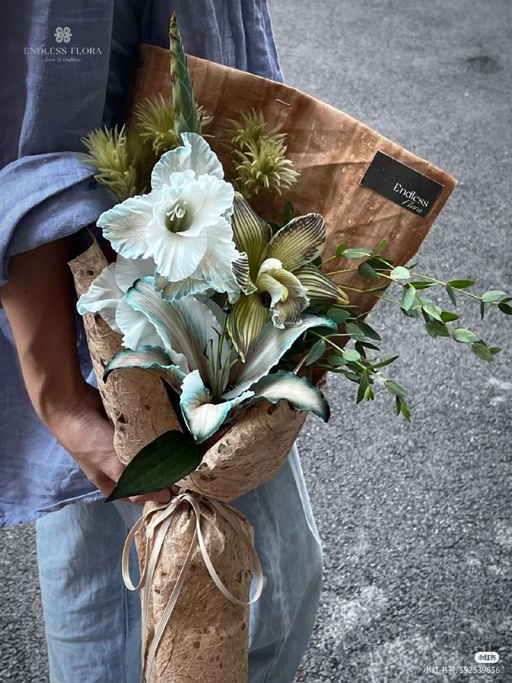 a person holding a bouquet of flowers in their hands on the street side, with a brown paper bag tied around them