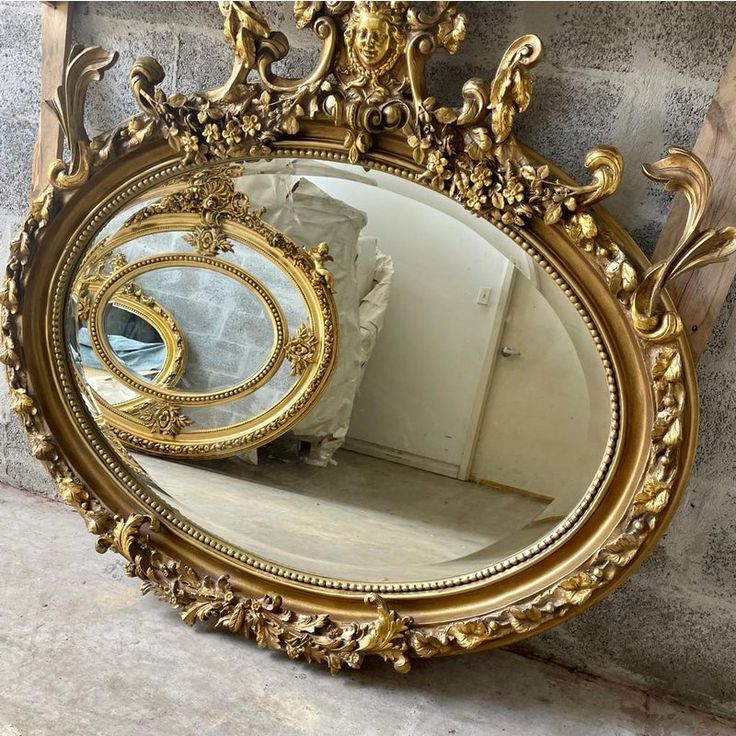 an ornate gold framed mirror sitting on the floor in front of a stone wall,