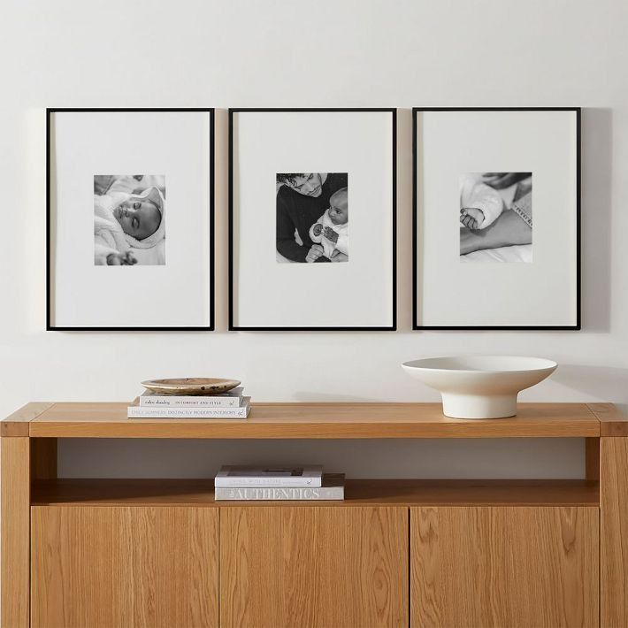 three black and white photographs hang on the wall above a wooden cabinet in a living room