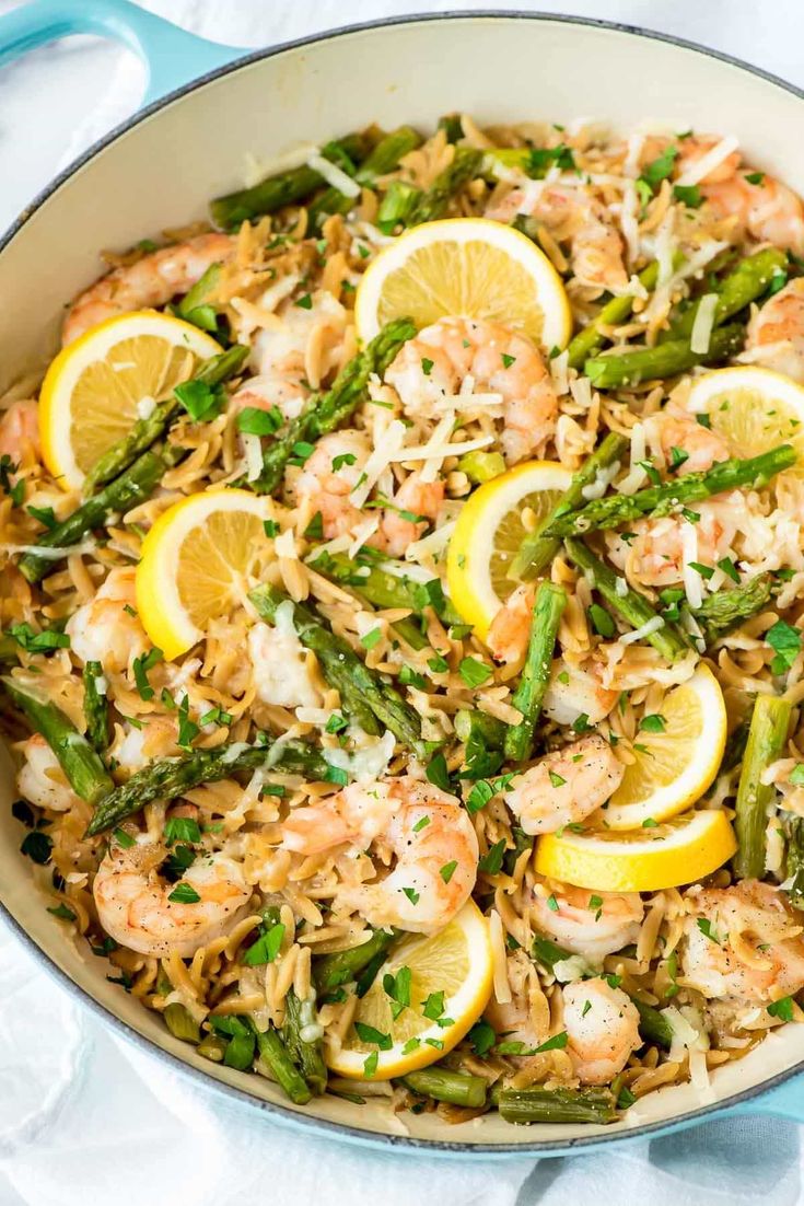 a skillet filled with shrimp, asparagus and lemons on top of rice