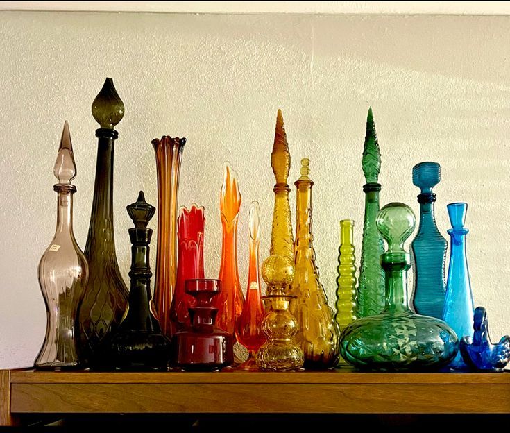 there are many different colored glass vases on the shelf