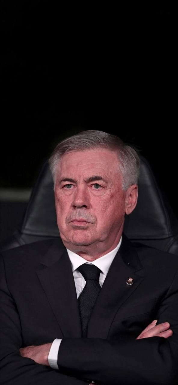 an older man wearing a suit and tie sitting in a chair with his arms crossed