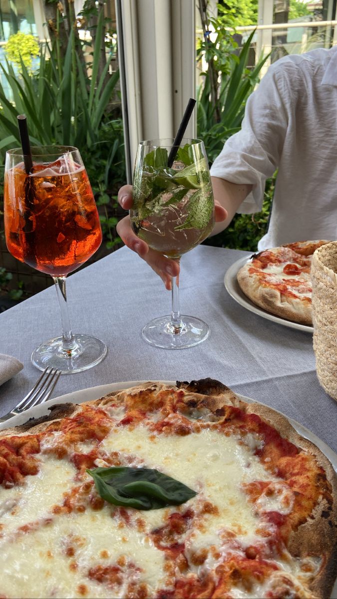 two pizzas sitting on top of a table next to glasses of wine and drinks