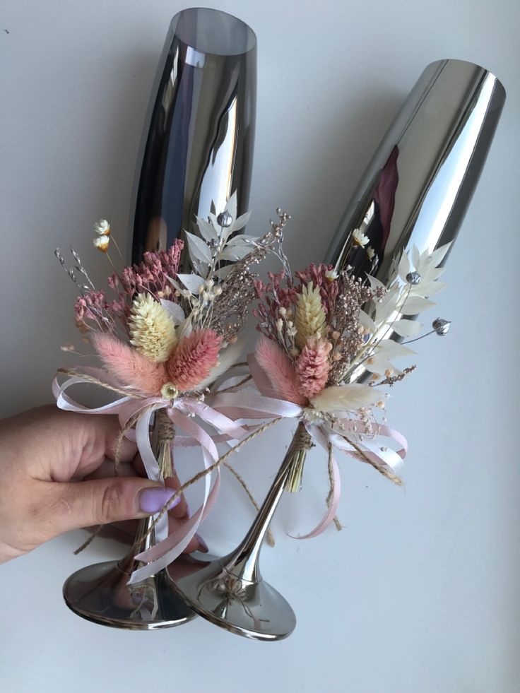 a person is holding two wine glasses with flowers in them and ribbons tied around the stems