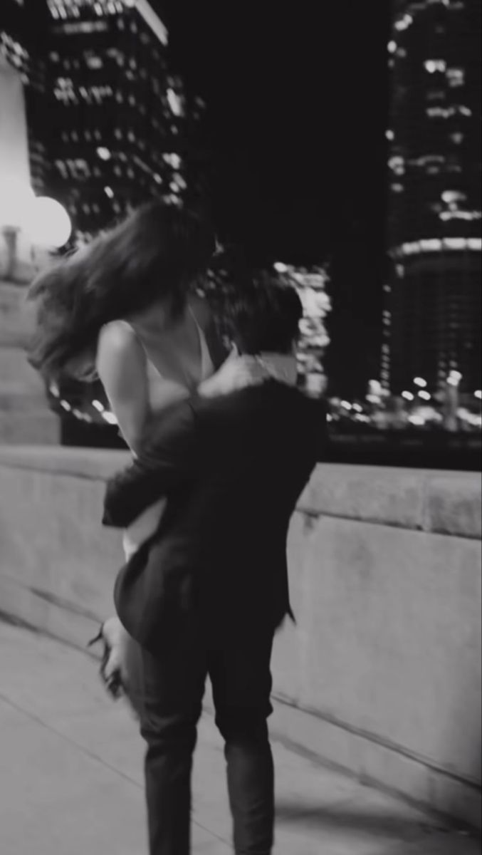 black and white photograph of a man hugging a woman on the sidewalk in front of a cityscape