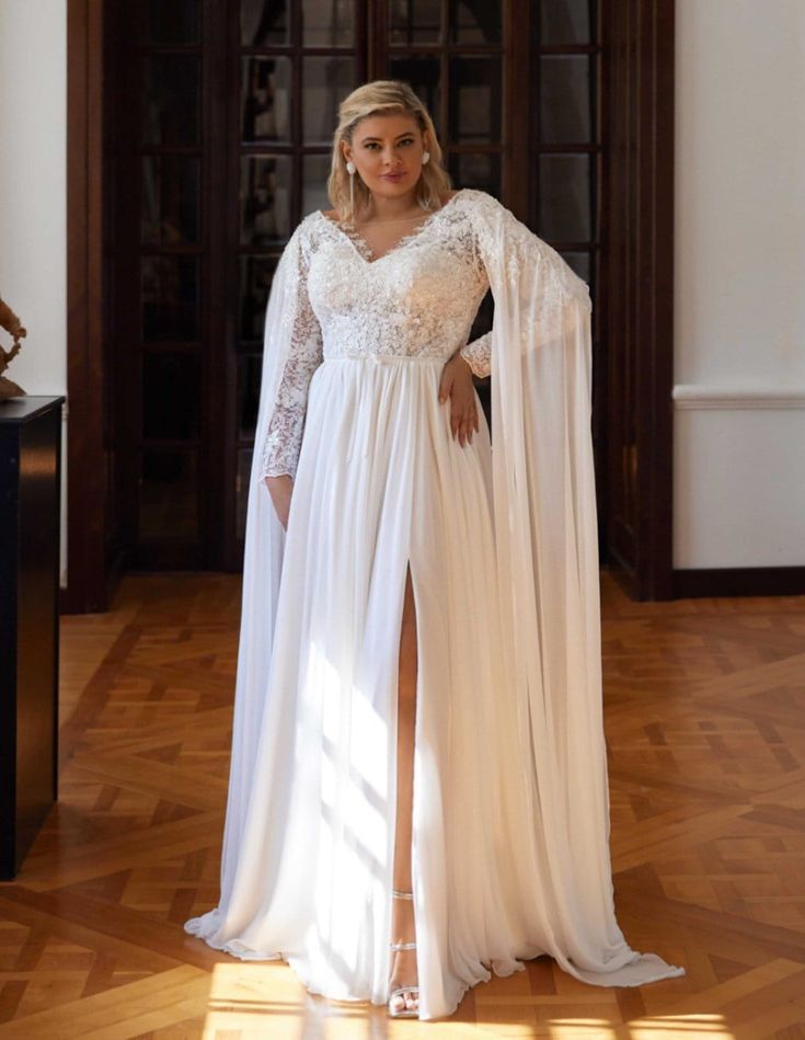 a woman wearing a white dress and cape standing in front of a door with her hands on her hips