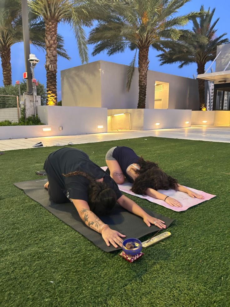 two people laying on yoga mats in front of a building with palm trees and lights