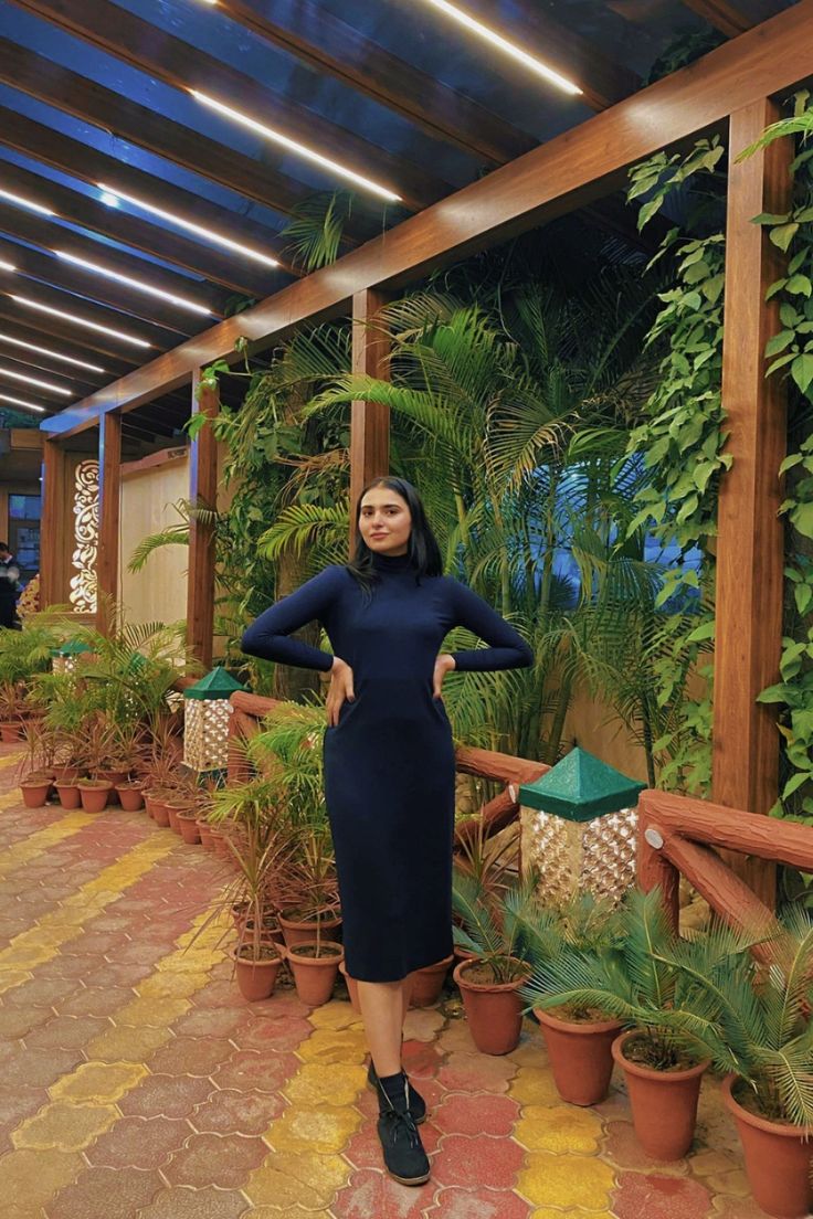 a woman is standing in front of some potted plants and posing for the camera