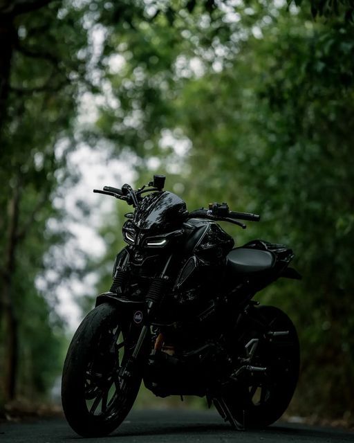 a black motorcycle parked on the side of a road in front of some green trees