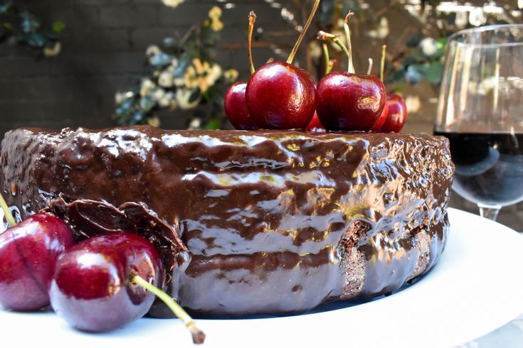 a chocolate cake with cherries on top next to a glass of wine and some branches