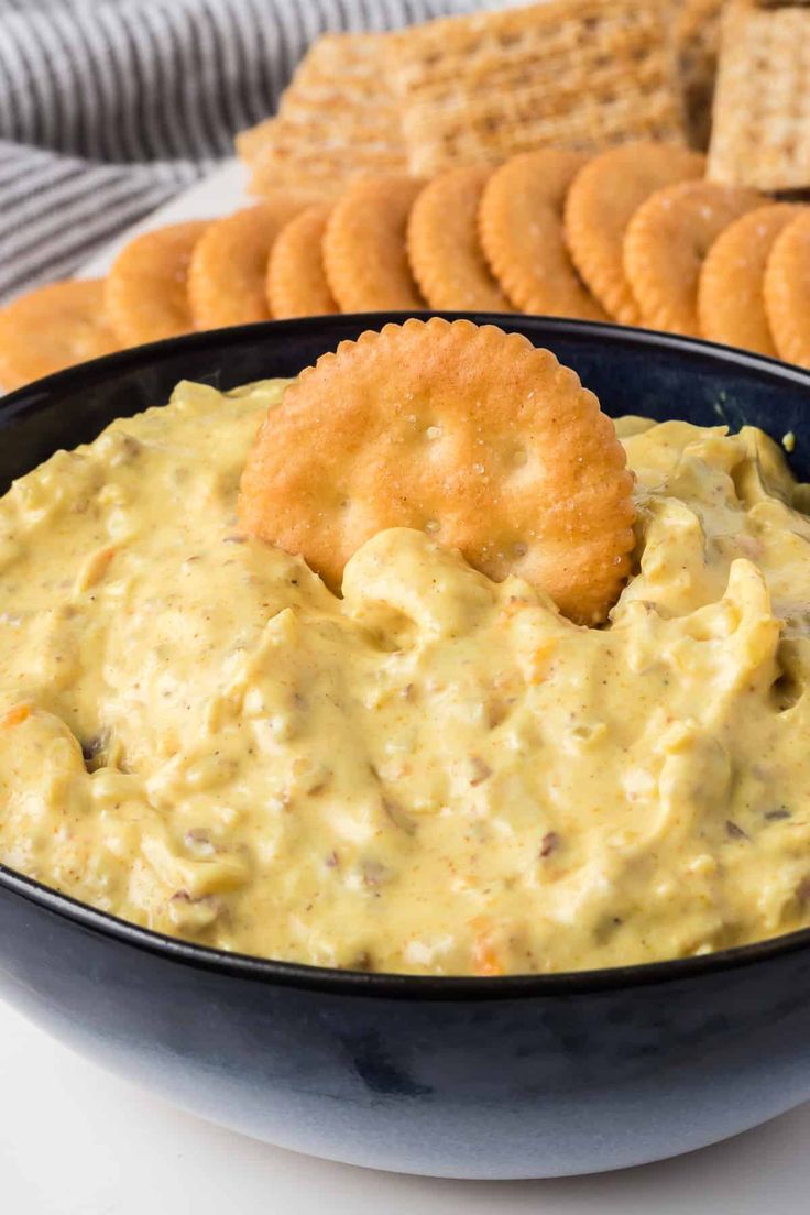 a black bowl filled with dip and crackers next to some crackers on the side