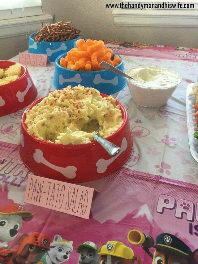 a table topped with lots of food on top of a pink cloth covered tablecloth