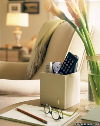 a vase with flowers and remotes in it sitting on a table next to a couch