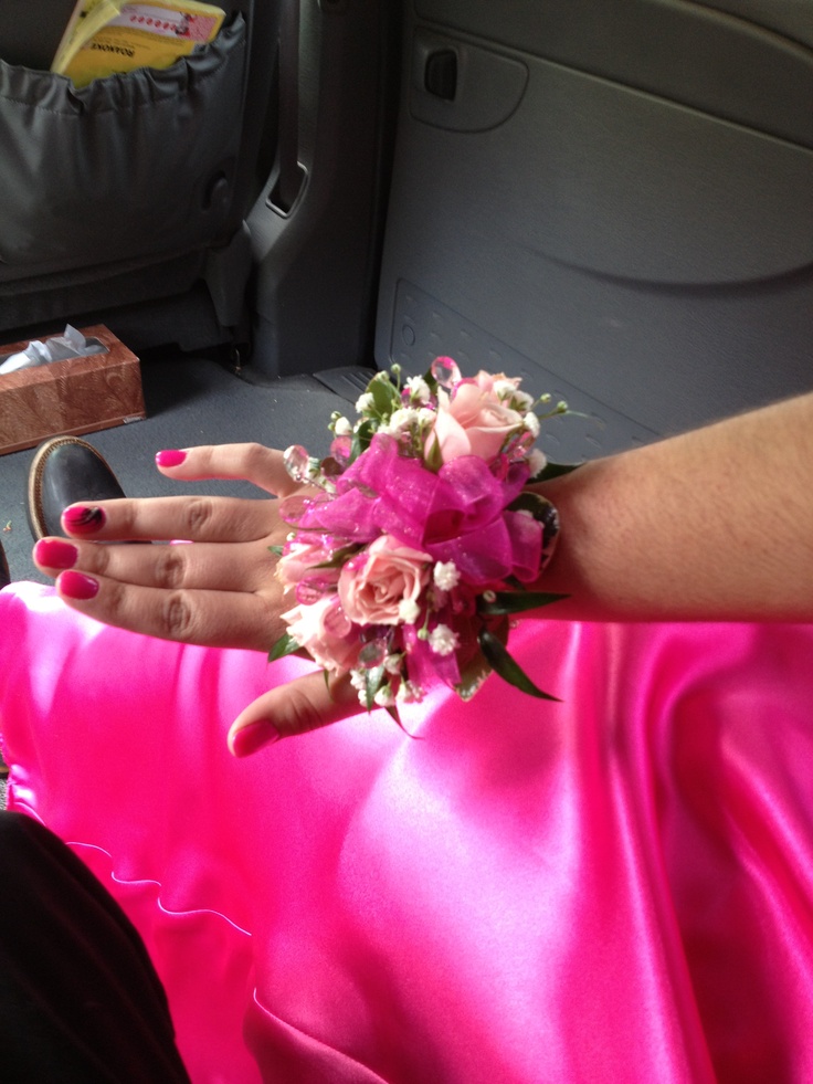 a woman in a pink dress with flowers on her wrist and hand resting on the seat