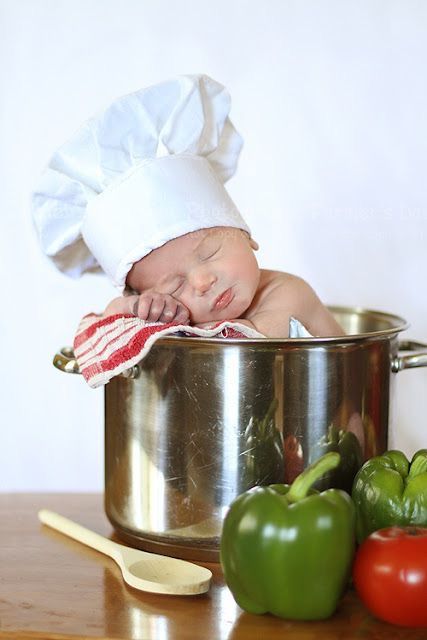 a baby in a chef's hat is sleeping in a pot next to vegetables