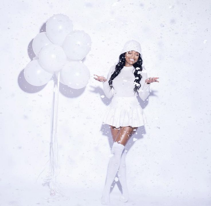 a woman standing in the snow with her arms out and balloons behind her, all around her