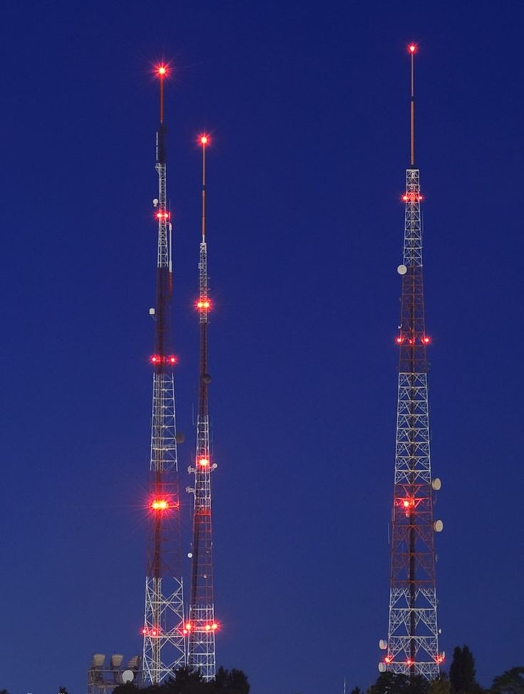 two very tall cell towers sitting next to each other in the dark blue night sky