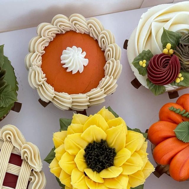 several cupcakes decorated with flowers and leaves on a white tablecloth, including pumpkins