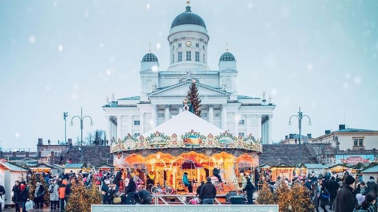 a merry christmas market in front of a large white building with lots of people around it