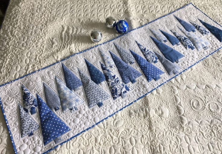 a quilted table runner with blue and white trees on it, surrounded by ornaments