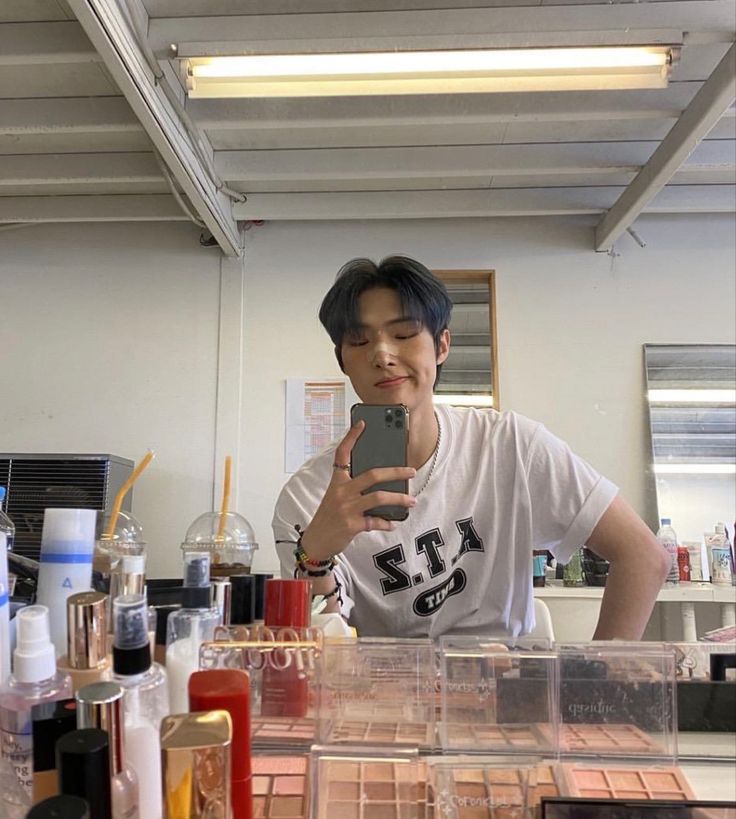 a young man taking a selfie in front of a counter full of makeup products