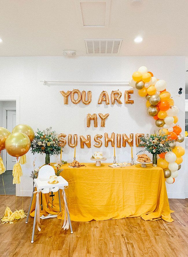 a table topped with yellow and orange balloons next to a sign that says you are my sunshine