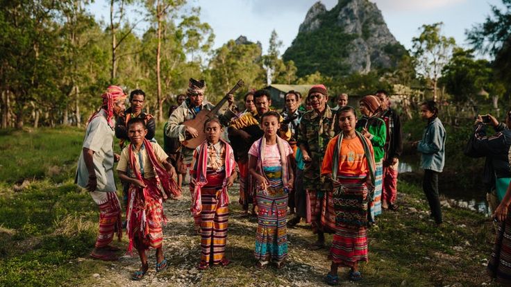 a group of people standing next to each other in front of a mountain side forest