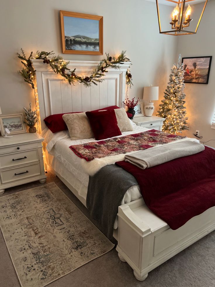 a white bed topped with pillows and blankets next to a christmas tree in a bedroom