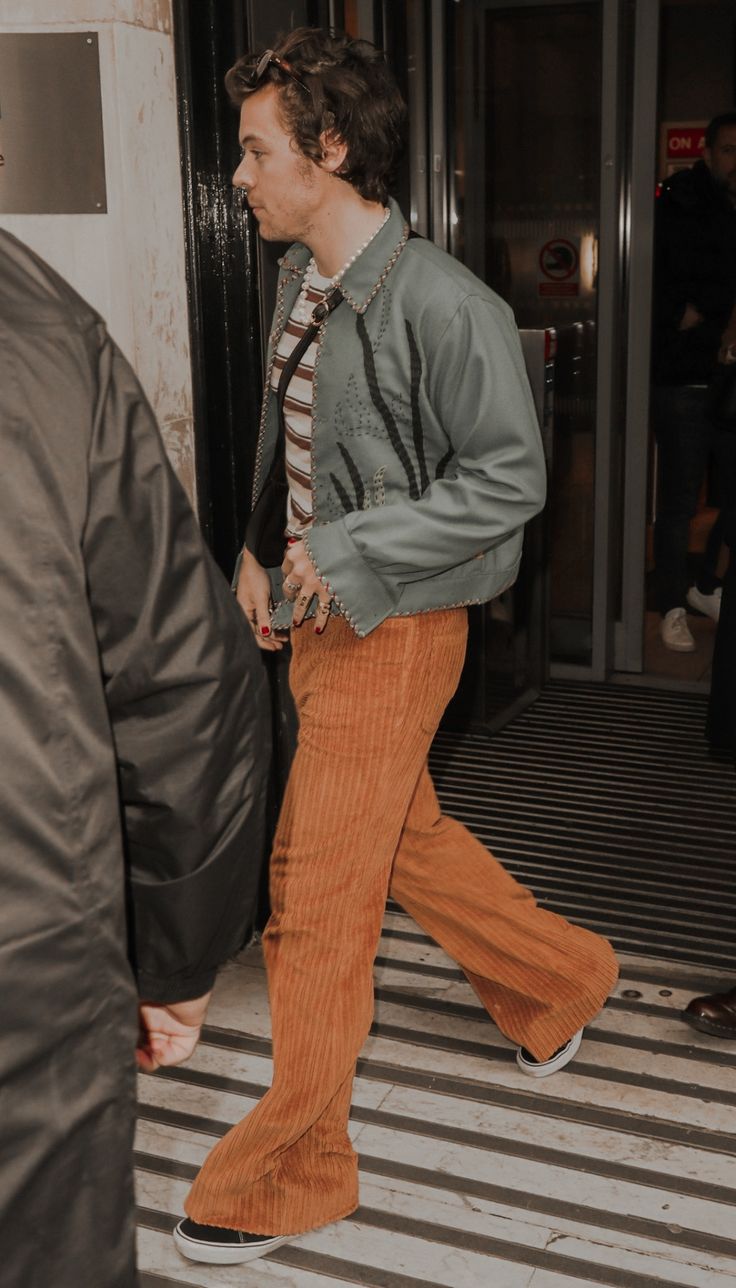 a man walking down the street in brown pants and a green jacket with black letters on it