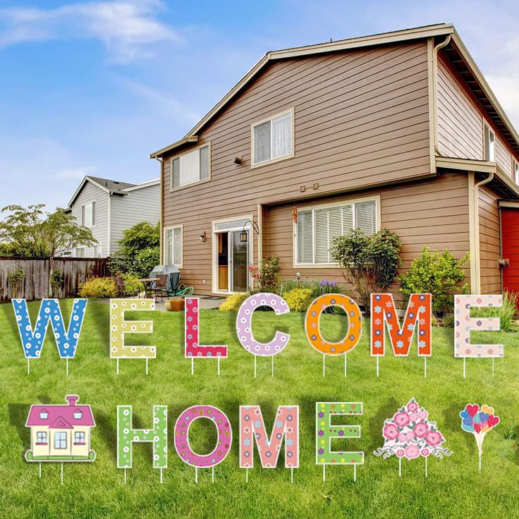 a welcome home sign in front of a house with flowers and houses on the lawn