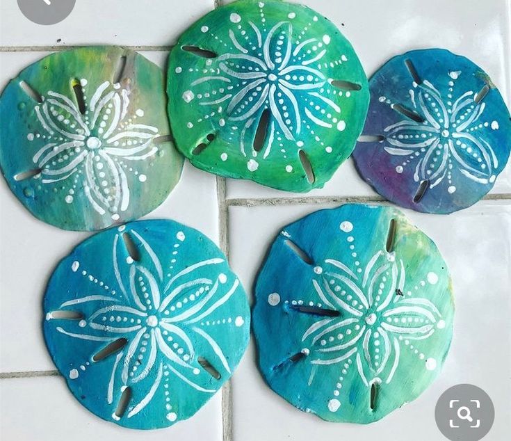 four sand dollars sitting on top of a white tile floor covered in blue and green designs