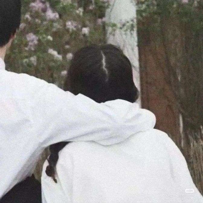 two people standing next to each other in front of a tree and flower covered area