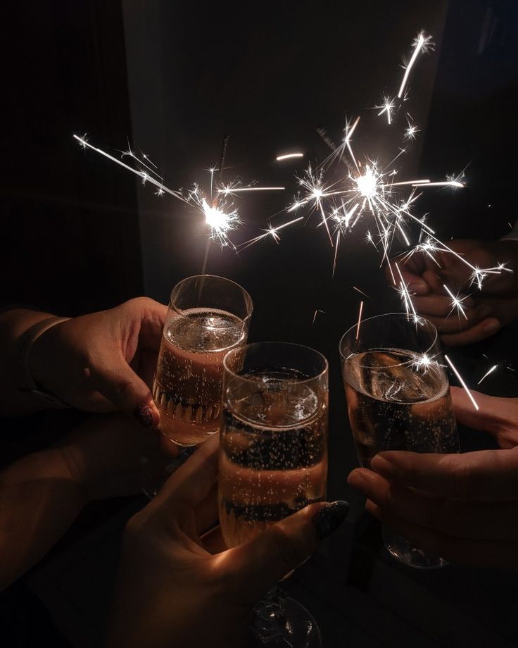 three people toasting with sparklers in their hands and holding glasses filled with champagne