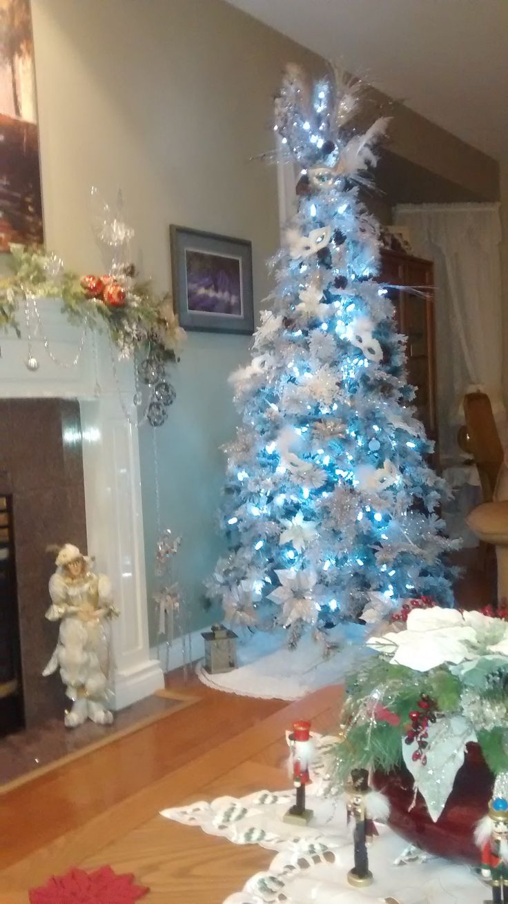 a white christmas tree with blue lights in a living room next to a fire place