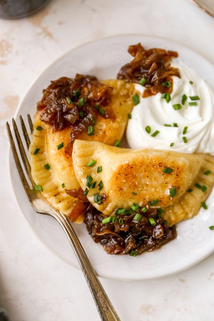 a white plate topped with two pastries covered in sauce and sour cream next to a fork