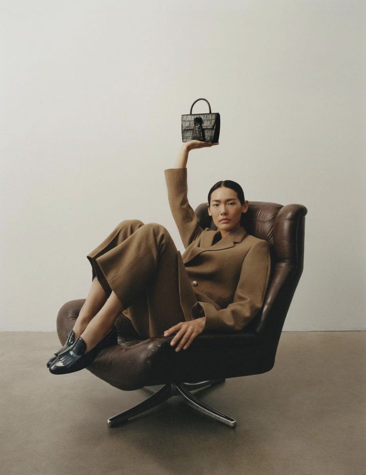 a woman sitting in a chair holding up a small object above her head with one hand